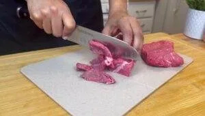 Person slicing raw beef on a cutting board with a sharp kitchen knife.