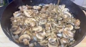 Sautéed mushrooms and onions in a cast iron skillet on a wooden surface, perfect for savory recipes.