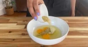 Mixing eggs, herbs, and cheese in a bowl on a wooden kitchen counter.