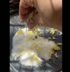 Hand mixing lemon zest and sugar on a black surface, creating a zest-infused sugar blend.