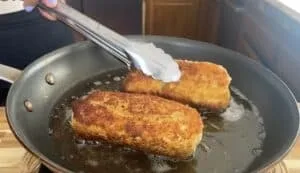 Golden brown fried bread rolls cooking in a pan, flipped with tongs for perfect crispiness.