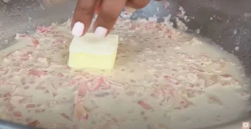 Adding butter to creamy onion sauce in a pan, enhancing flavor and texture.