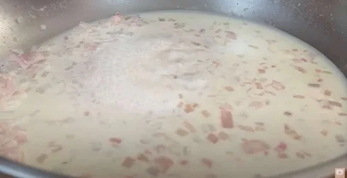 Creamy sauce with diced onions and ham simmering in a pan.