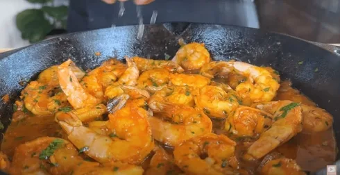 Sizzling peri peri shrimp in garlic tomato sauce with herbs in a cast iron skillet, a flavorful seafood delicacy being garnished.