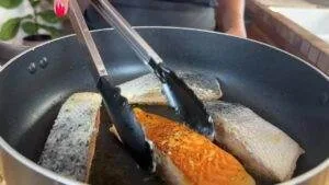 Cooking salmon fillets in a pan with tongs, showing crisp and golden-brown texture. Perfect for a healthy meal.