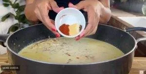 Adding spices to creamy soup in a pan, enhancing flavor with a mix of paprika, garlic powder, and seasonings.