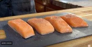 Four seasoned salmon fillets on a black cutting board, ready for cooking in a kitchen.