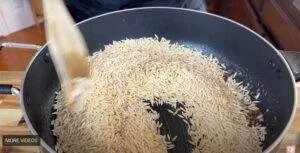 Toasting orzo pasta in a black skillet, wooden spoon stirring for a perfect golden texture.