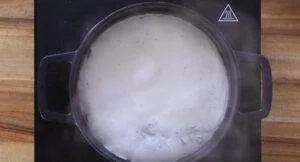 Pot of milk boiling on a stovetop, creating steam, viewed from above.