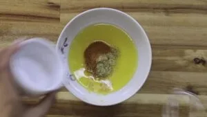 Mixing spices into melted butter in a white bowl on a wooden surface.