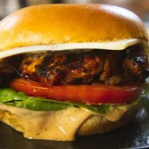 Close-up of a juicy grilled chicken sandwich with fresh lettuce, tomato, and creamy sauce on a toasted brioche bun.