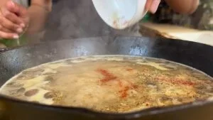 Adding seasonings to a simmering pan for a flavorful dish. Perfect for enhancing savory recipes with aromatic herbs.