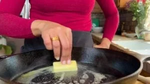 Person melting butter in a hot skillet with a red top, in a cozy kitchen.